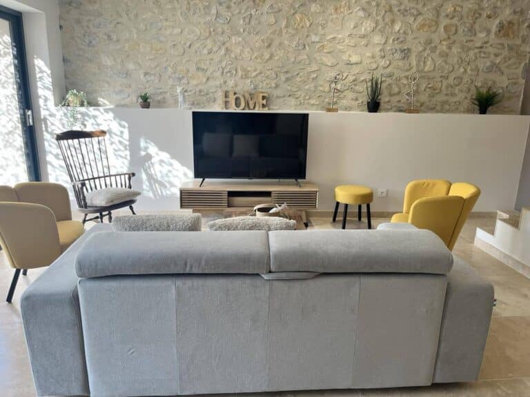 Bright living room of the cottage Le Chant des Mésanges with stone wall, comfortable sofa and TV.